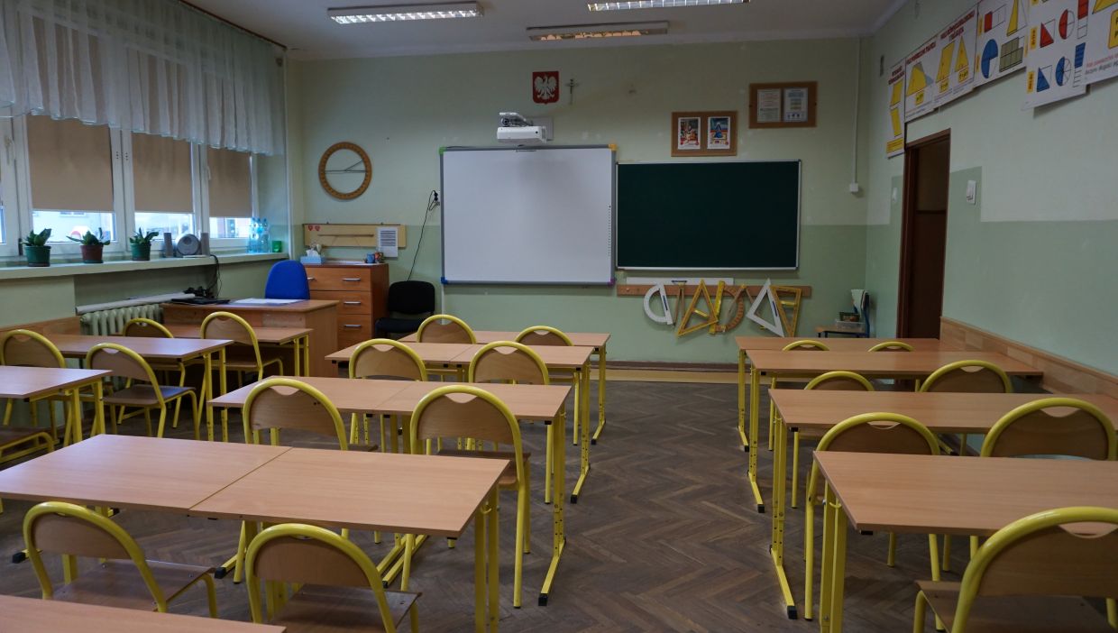 Sala matematyczna. Sala lekcyjna z żółtymi krzesłami, tablicą i przyrządami geometrycznymi na ścianie.