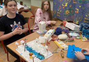 Uczennice tworzą makietę zimowej Narnii, wykorzystując watę, karton i niebieskie elementy symbolizujące rzekę.