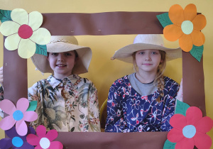 Dziewczynki w kapeluszach pozują w ozdobnej ramce podczas zajęć związanych z Dniem Babci i Dziadka.