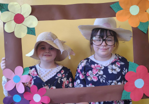 Dziewczynki w kapeluszach pozują w ozdobnej ramce podczas zajęć związanych z Dniem Babci i Dziadka.