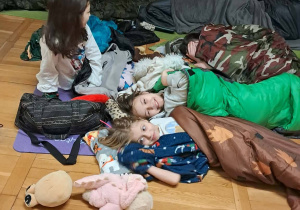 Uczniowie siedzą i leżą w śpiworach podczas wieczornych rozmów.