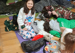 Uczniowie leżą w śpiworach na materacach w klasie podczas nocowania w szkole.