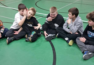 Uczniowie siedzą w kręgu, jeden z nich szepcze coś do ucha kolegi.