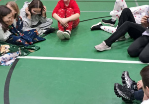 Uczniowie siedzą w kręgu na sali gimnastycznej podczas zabawy integracyjnej.