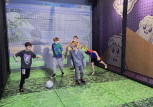 Uczniowie grają w interaktywną grę piłkarską na wirtualnym boisku.