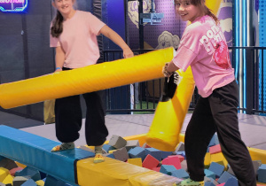 Dwie uczennice stoją na równoważni nad basenem z gąbkami.