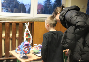 Kobieta i chłopiec stoją przy stole z modelami biologicznymi i przyglądają się wykonanym pracom.