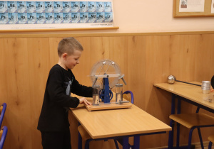 Chłopiec stoi przy szkolnym urządzeniu do doświadczeń fizycznych i obserwuje jego działanie.