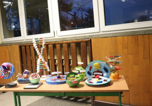 Modele komórki i DNA wykonane przez uczniów stoją na stole w szkolnym korytarzu.