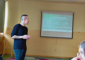 Marcin Józefaciuk prowadzi prelekcję dla uczniów w klasie; na ekranie widoczna jest prezentacja dotycząca hejtu.