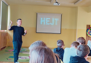 Marcin Józefaciuk przemawia do uczniów; za nim wyświetlona jest prezentacja na temat hejtu.