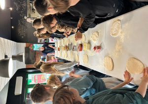 Uczniowie klasy VIIa przygotowują ciasto do pizzy przy wspólnym stole.