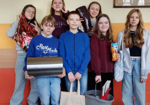 Grupa uczniów trzyma książki w nietypowych przedmiotach, m.in. w wiadrze i metalowym pudełku.