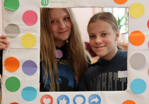 Dwie uczennice klasy 6a ze Szkoły Podstawowej nr 13 w Pabianicach pozują w kolorowej ramce z napisem „Dzień Kropki”. Obie dziewczynki uśmiechnięte, w tle widoczne klasyczne wnętrze sali lekcyjnej.
