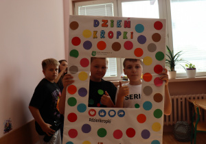 Uczniowie klasy 6a z SP13 w Pabianicach pozują w ramce ozdobionej kolorowymi kropkami z napisem „Dzień Kropki”. Dwóch chłopców pokazuje uniesione kciuki.