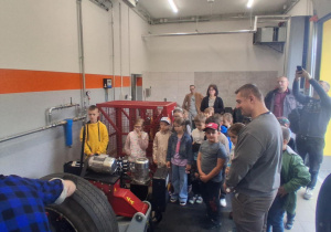Klasa 2B z SP 13 obserwuje pracę wulkanizatora w MZK Pabianice. Uczniowie poznają sprzęt i zawody związane z komunikacją miejską. Z tyłu nauczycielki i opiekunowie.
