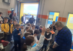 Uczniowie SP 13 podczas warsztatów w MZK słuchają wulkanizatora. Jedno z dzieci podnosi rękę. W tle nauczycielki Monika Juran-Tłoczek i Monika Mettler.