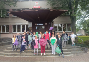 Uczniowie SP13 stoją przed wejściem do szkoły z workami pełnymi śmieci po zakończonej akcji Sprzątania Świata, widoczna tablica z nazwą szkoły.