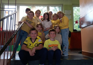 Grupa dzieci z klasy 2b w czerwonych ubraniach pozuje z wychowawczynią Moniką Mettler w klasie podczas szkolnej akcji „Dzień Koloru”. W tle mapy i dekoracje ścienne.