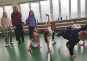 Dzieci ćwiczą na sali gimnastycznej podczas Dnia Integracji. Troje uczniów wykonuje zabawy ruchowe w podporze, a cztery starsze dziewczynki obserwują i prowadzą zajęcia.