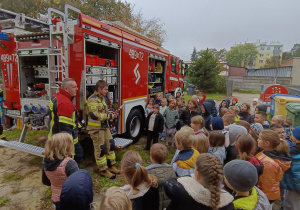 Dzieci z klasy II stoją w skupieniu przy otwartym wozie strażackim, słuchając strażaków z OSP Pabianice prezentujących sprzęt ratowniczy.