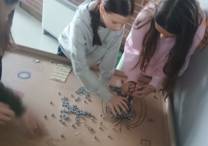 Uczennice przeprowadzają eksperyment z magnesami i metalowymi elementami na stole w Centrum Nauki EC1.