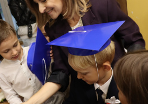 Pani Agnieszka Jarzębowska wita pierwszoklasistów w niebieskich biretach po ślubowaniu.