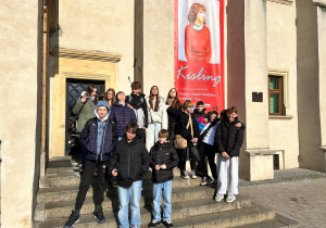 Uczniowie klasy 7a stoją przed wejściem muzeum w Pabianicach na tle baneru wystawy „Kisling w Pabianicach”.