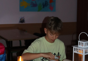 Brajan z klasy 7b siedzi przy świecach i lampionie podczas wieczornego czytania „Dziadów” Mickiewicza w nastrojowej sali.