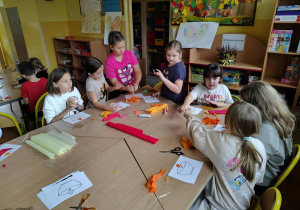 Dzieci w świetlicy siedzą przy stolikach i wykonują jesienne prace plastyczne z bibuły i papieru.