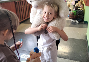 „Uśmiechnięty uczeń na korytarzu szkoły niesie na plecach wielkiego białego misia podczas Dnia Pluszowego Misia.”