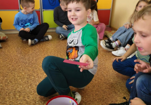 Uczeń klasy 1b losuje karteczkę z wróżbą z czerwonego kapelusza, otoczony kolegami podczas andrzejkowej zabawy w klasie.