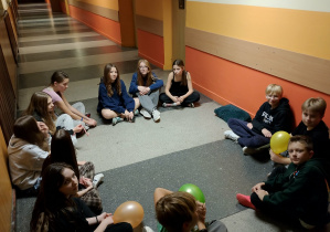 Grupa szóstoklasistów siedzi w kręgu na korytarzu, rozmawia i trzyma balony w czasie andrzejkowego nocowania.