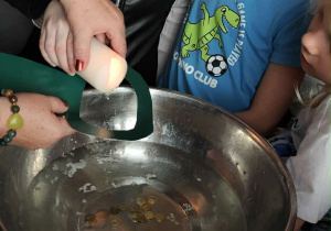 Uczennica klasy 2a, trzymając świecę nad metalową miską z wodą, leje wosk podczas andrzejkowej wróżby, a obok niej przyglądają się inne dzieci.