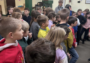 Dzieci z klas drugich słuchają przewodniczki podczas zwiedzania fabryki bombek.