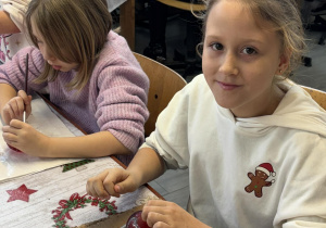 Dwie dziewczynki z klas 2a i 2b dekorują czerwone bombki brokatem przy stole w pracowni fabryki bombek w Piotrkowie Trybunalskim.