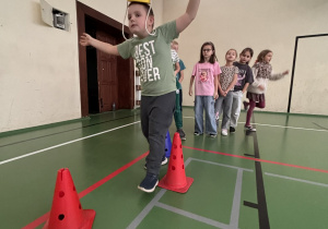 Uczeń przechodzi slalom między pachołkami, balansując żółtym kaskiem na głowie podczas Świetlicowej Olimpiady Sportowej.