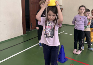 Dziewczynka zakłada żółty kask przed startem w slalomie między pachołkami podczas Świetlicowej Olimpiady Sportowej.