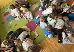 Grupy dzieci siedzą na kolorowym dywanie w świetlicy i budują wspólne konstrukcje z kredek i klocków podczas listopadowych zajęć integracyjnych.