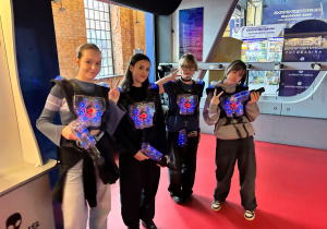 Uczennice klasy 7a w świecących kamizelkach i z pistoletami laserowymi stoją przy wejściu do areny, gotowe do udziału w grze.