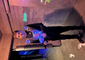 Uczeń 7a w kamizelce laserowej stoi na arenie Laser Games i trzyma pistolet, gotowy do gry.