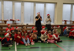 Uczniowie klas I–VI w czapkach Mikołaja na sali gimnastycznej; w tle nauczycielki SP 13.