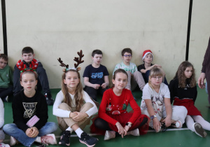 Starsze dzieci siedzą na sali gimnastycznej i oglądają program Mikołajek.