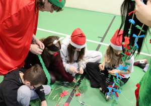 Uczniowie z nauczycielką SP 13 wykonują świąteczny łańcuch podczas Mikołajek.