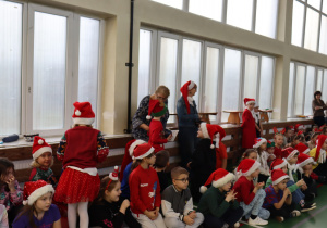 Zgromadzeni uczniowie w świątecznych czapkach podczas Mikołajek; w tle nauczycielki SP 13.