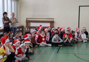 Uczniowie obserwują mikołajkowy program na sali gimnastycznej; obok nauczycielki SP 13.