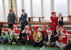 Uczniowie w mikołajkowych strojach na sali gimnastycznej; w tle nauczycielki SP 13.