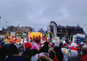 Tłum mieszkańców ogląda iluminowaną platformę z Mikołajami i świątecznymi dekoracjami na Pabianickim Jarmarku Świątecznym.