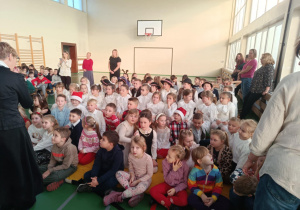 Uczniowie klas 1–3 siedzą w sali gimnastycznej podczas szkolnej uroczystości.