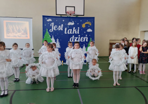 Uczennice klas młodszych w białych strojach prezentują taniec z wiankami podczas koncertu świątecznego.